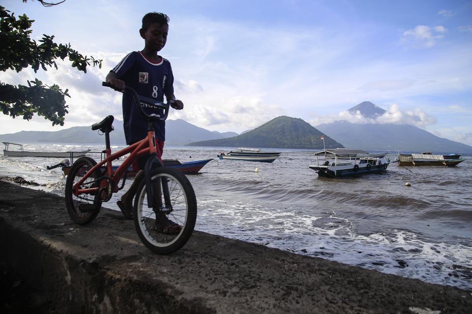 Seorang anak mendorong sepedanya di dekat perahu nelayan yang lego jangkar saat tidak melaut di Pantai Fitu, Ternate, Maluku Utara, Sabtu (13/7/2024). Sebagian nelayan kecil di daerah itu memilih tidak melaut sejak sepekan terakhir setelah BMKG setempat 