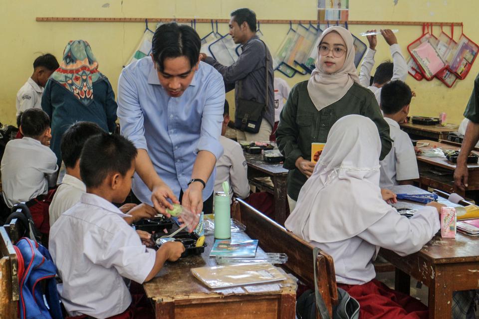 Wakil Presiden terpilih Gibran Rakabuming Raka membantu siswa membuka paket makanan saat meninjau uji coba pelaksanaan program makan bergizi gratis di SDN Sentul 03, Kabupaten Bogor, Jawa Barat, Selasa (23/7/2024). Program makan bergizi gratis dengan ang