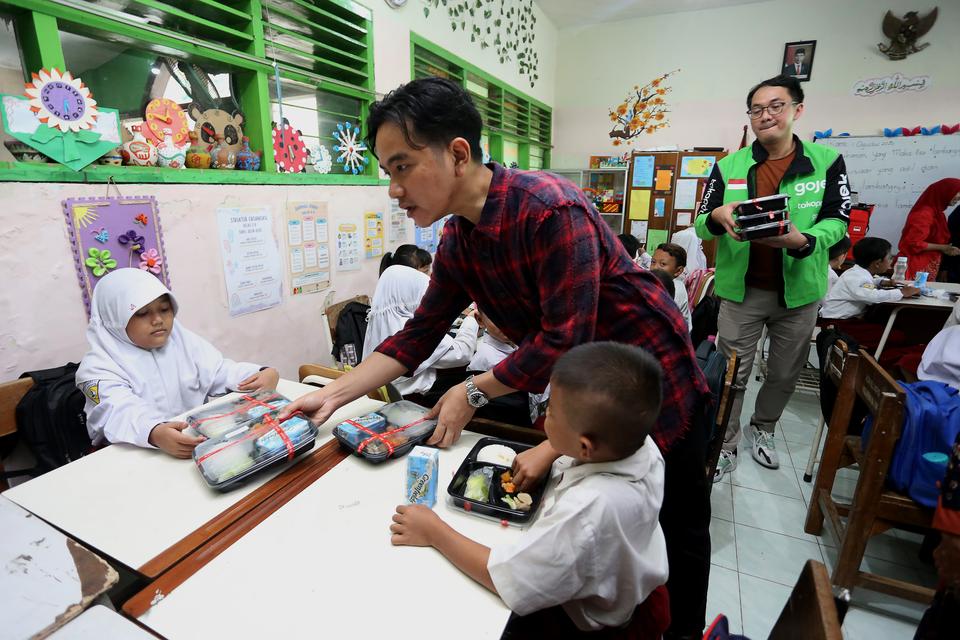 Wakil Presiden terpilih Gibran Rakabuming Raka (tengah) membagikan paket makanan saat meninjau uji coba pelaksanaan program makan bergizi gratis di SD Negeri Klampis Ngasem 3, Surabaya, Jawa Timur, Kamis (1/8/2024). Uji coba program makan bergizi gratis d