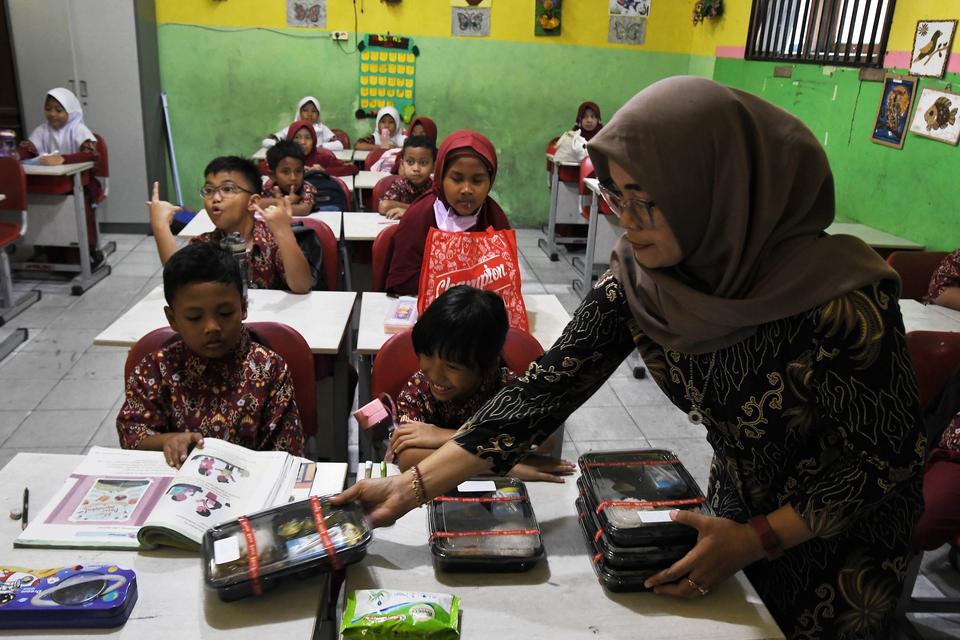 Seorang guru (kanan) membagikan makanan ke murid saat uji coba makan bergizi gratis di SDN Teluk Pucung VII, Bekasi, Jawa Barat, Kamis (15/8/2024). Uji coba program makan gratis selama satu bulan di sekolah tersebut sebagai upaya dalam memenuhi asupan mak