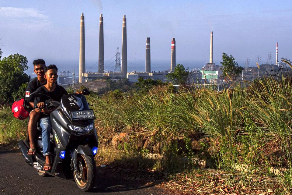 Pengendara sepeda motor melintas di sekitar Pembangkit Listrik Tenaga Uap (PLTU) Suralaya, Cilegon, Banten, Minggu (8/9/2024). Kementerian Energi dan Sumber Daya Mineral (ESDM) berencana menghentikan operasional 13 unit PLTU di Indonesia termasuk di antar