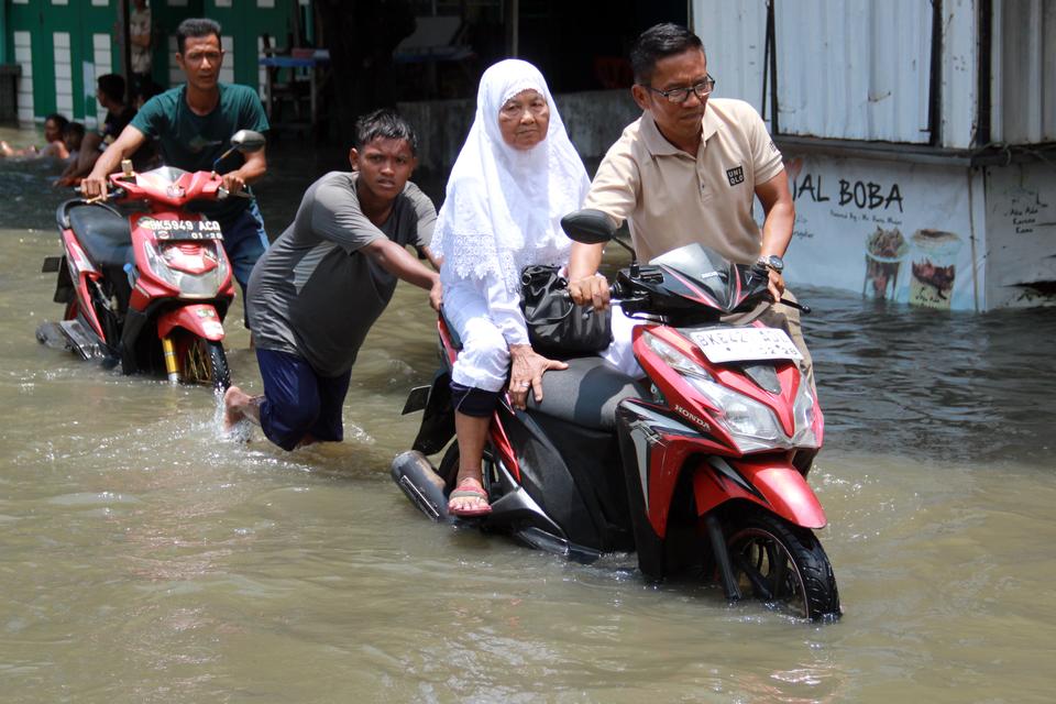 Sejumlah warga mendorong sepeda motornya melintasi banjir di Kelurahan Martubung, Medan Labuhan, Medan, Sumatera Utara, Minggu (15/9/2024). 