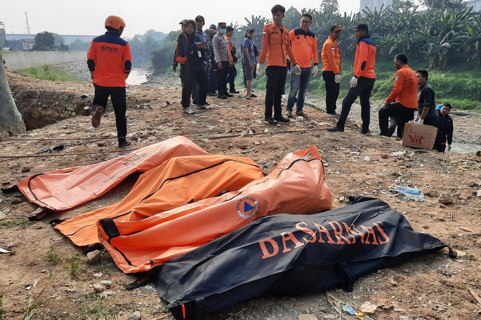 Sejumlah petugas BPBD Kota Bekasi dan polisi berdiri dengan latar depan kantong-kantong berisi tujuh jenazah laki laki yang ditemukan mengambang di Kali Bekasi, Pondok Gede Permai, Jatiasih, Kota Bekasi, Minggu (22/9/2024). Kepolisian masih menyelidiki p