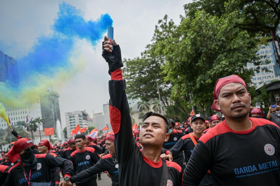 Sejumlah buruh menyalakan suar saat berunjuk rasa di kawasan Patung Kuda, Jakarta, Kamis (24/10/2024). Mereka meminta pemerintah untuk menaikkan upah minimum tahun 2025 sebesar 8 hingga 10 persen serta menuntut pencabutan Omnibus Law atau UU Cipta Kerja k