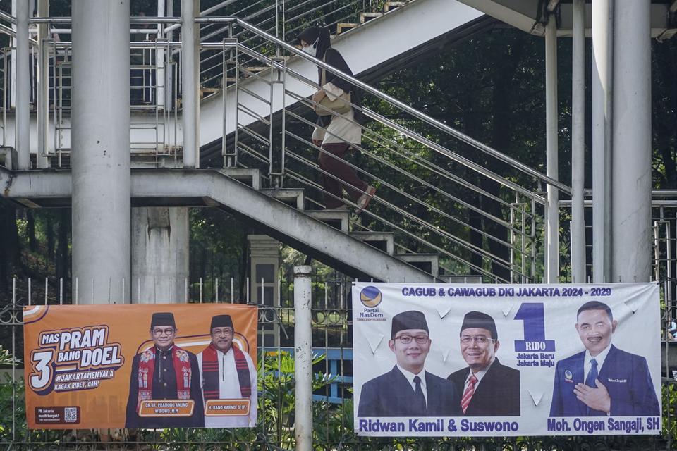 Warga berjalan melalui Jembatan Penyeberangan Orang (JPO) di dekat Alat Peraga Kampanye (APK) Pilkada Jakarta yang terpasang di Halte Flyover Jatinegara, Jakarta.