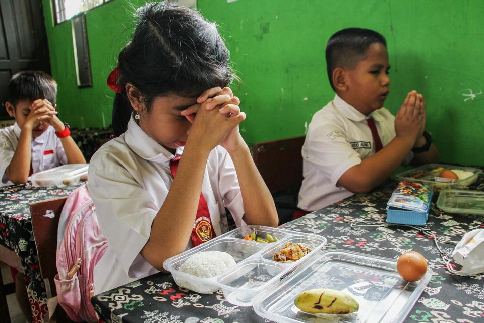 Sejumlah siswa berdoa sebelum menyantap makan bergizi gratis di SD Negeri 1 Bukit Tunggal, Palangka Raya, Kalimantan Tengah, Senin (13/1/2025).