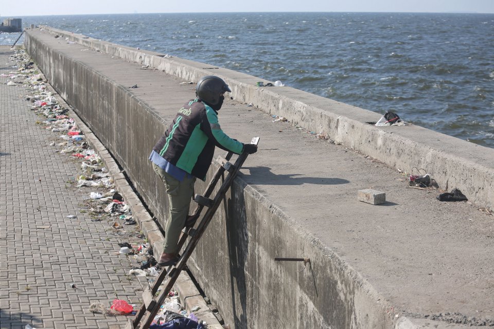 Pengemudi ojek online menaiki tangga yang berada di tanggul laut di kawasan Muara Baru, Penjaringan, Jakarta Utara, Senin (17/6/2025). 