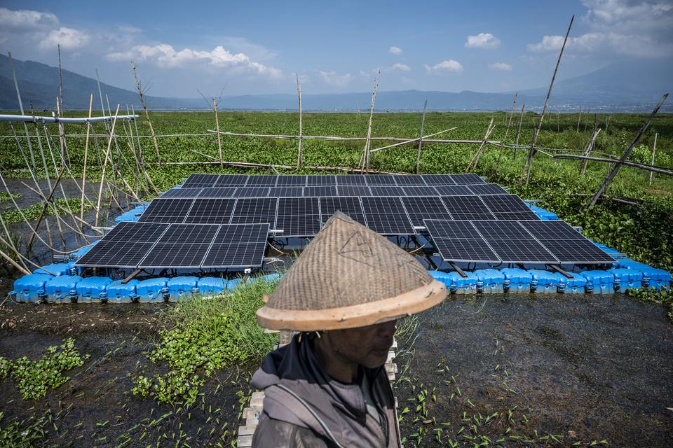 Petani berada di dekat panel surya yang terpasang di Pembangkit Listrik Tenaga Surya (PLTS) Terapung Rawa Pening, Desa Kesongo, Tuntang, Kabupaten Semarang, Jawa Tengah, Minggu (12/10/2025). 