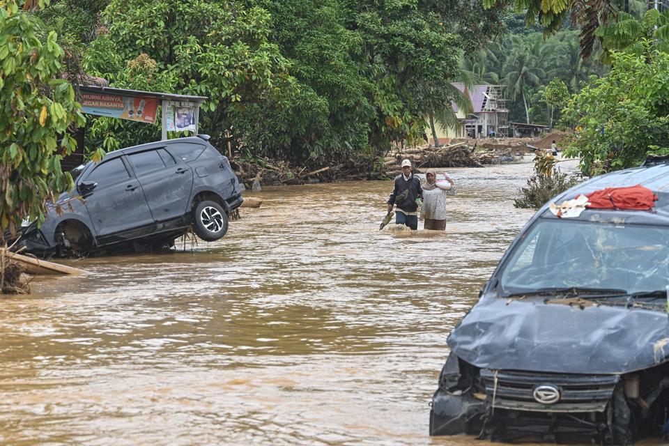Warga melintasi banjir yang menggenangi permukiman penduduk di Kelurahan Tukka, Kecamatan Tukka,Tapanuli Tengah, Sumatera Utara, Minggu (7/12/2025). 
