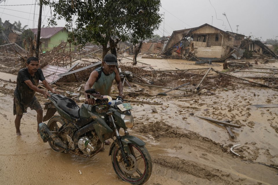 Warga mendorong sepeda motor melintas di desa yang luluh lantak pascabanjir di Desa Bundar, Karang Baru, Kabupaten Aceh Tamiang, Aceh, Selasa (9/12/2025). BNPB bersama Kementerian Kesehatan memastikan layanan rumah sakit pemerintah di Aceh, Sumut, dan Sum