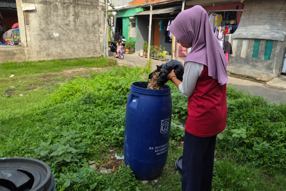 Tina, koordinator lapangan (korlap) dasawisma RW 07 Rorotan, membuang sampah organik berupa kulit pisang ke tong drop point sebagai bagian pemilahan sampah dari sumber di lingkungan warga, Rabu (20/5/2026). 