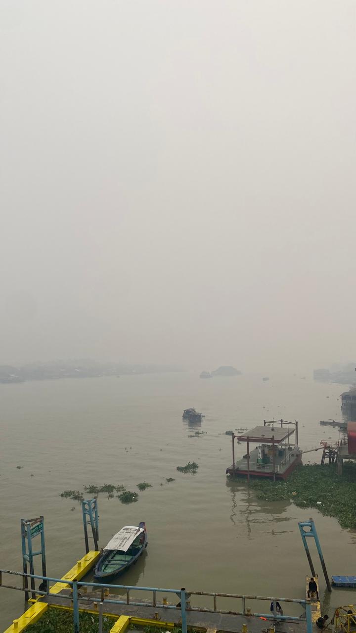 Sungai Musi di Palembang tertutup kabut asap; perahu tertambat di dermaga, seberang sungai nyaris tak terlihat.